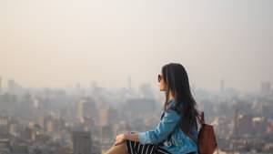 Junge Frau sitzt auf dem Dach eines Hauses und schaut in die Ferne 