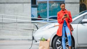 Frau steht vor Elektroauto und Tankt Strom - E-Mobilität 