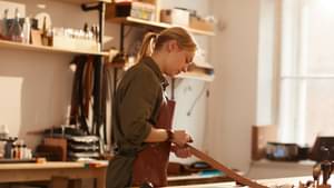 Eine Schreinerin steht in ihrer Werkstatt und bearbeitet ein Stück Holz.