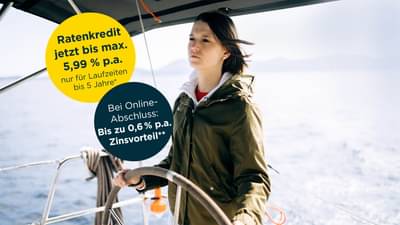 Junge Frau mit dunklen Haaren steht am Steuer eines kleinen Schiffs auf offenem Wasser: Darlehen bis 5,99% p.a.* und zusätzlichen Zinsvorteil bei Online-Abschluss von bis zu 0,6% p.a.**