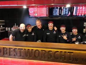 Lars Obendorfer Familie und seine Mitarbeiter stehen hinter der Theke einer Filiale und lachen in die Kamera