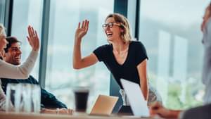 Eine Frau steht an einem großen Konferenztisch und gibt jemandem ein High-Five.