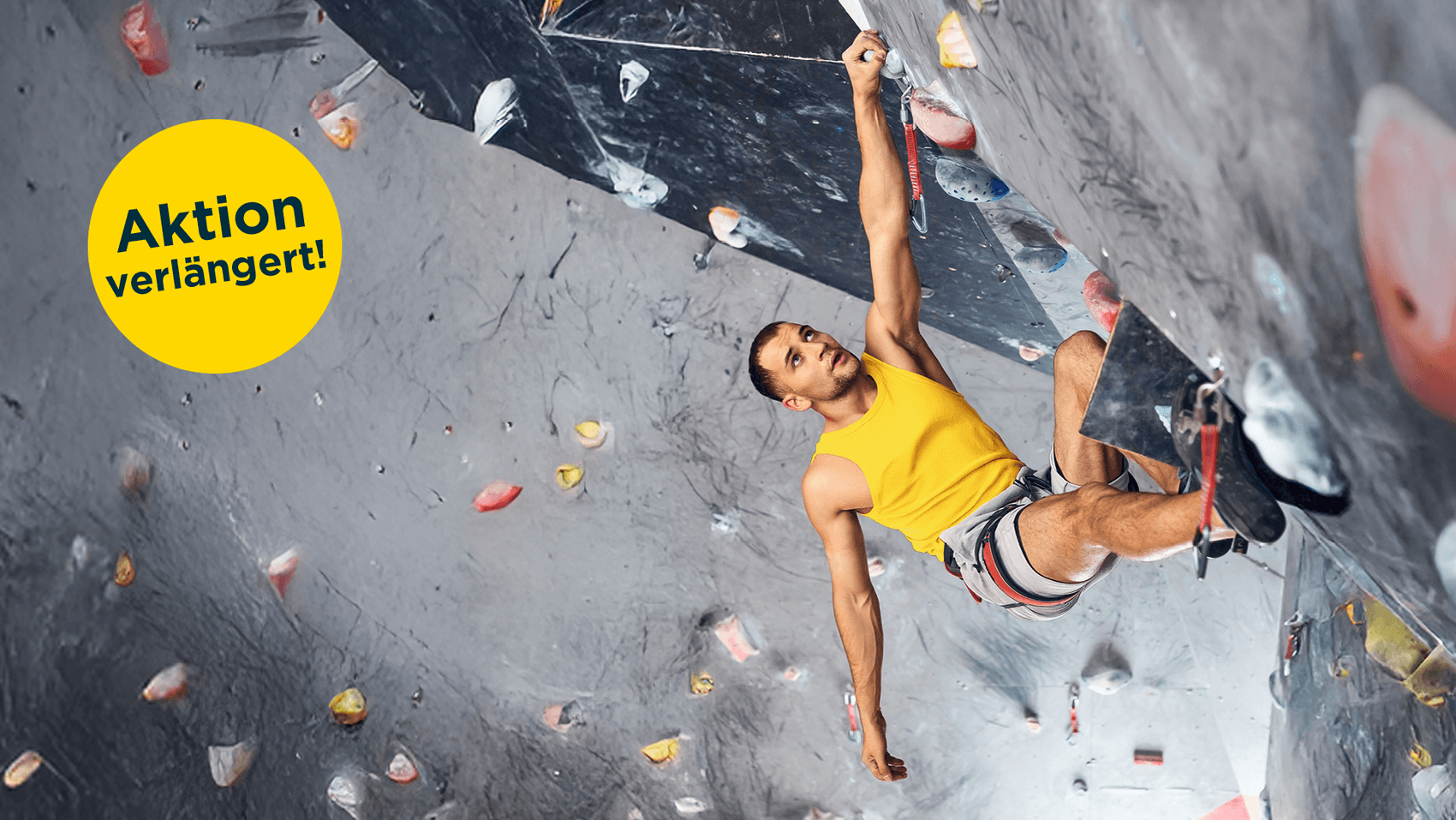 Ein Kletterer mit gelben ärmellosen Shirt hängt mit einer Hand an einer überhängenden Boulderwand..