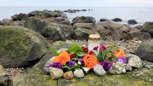 Eine kleine Gedenkstätte mit Kerze, Blumen und Steinen an einer Küste