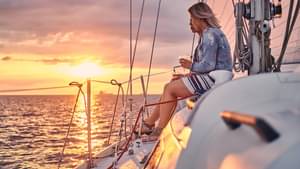 Zwei Frauen sitzen auf dem Decke eines Segelschiffes und schauen sich den Sonnenuntergang an.