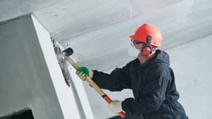 Handwerker in Schutzkleidung reißt mit einem großen Hammer eine Wand ein.