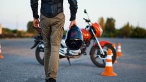 Ein Mann hält lässig einen Motorradhelm in der Hand und schlendert auf ein Motorrad zu.