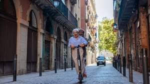 Ein älteres Pärchen fährt glücklich auf einem e-Roller durch eine Straße in einer Altstadt.