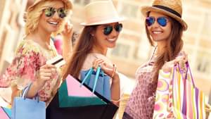 Drei junge Freundinnen mit Sonnenbrille und Hut gehen im Urlaub shoppen.