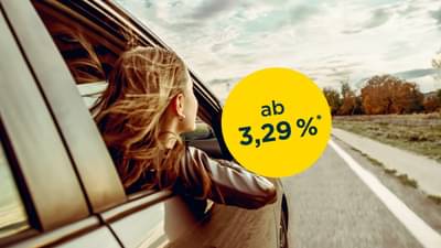 Junge Frau mit blonden Haaren sitzt auf der Beifahrerseite eines Autos und lehnt sich mit Arm und Kopf zum offenen Fenster raus: Autokredit ab 3,29% p.a.*