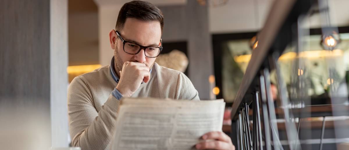 Ein nachdenklich schauender Mann sitzt am Tisch und liest aufmerksam eine Zeitung.