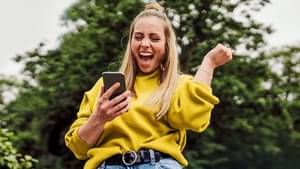 Frau schaut jubelnd auf ihr Handy