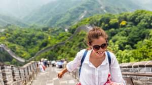Junge Frau mit Sonnenbrille, die die chinesische Mauer hinaufsteigt und dabei lächelt.