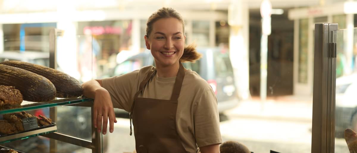 Sophie Hinkel lehnt entspannt lächelnd an einem Verkaufstresen für Brot in einer ihrer Bäckerei-Filialen.