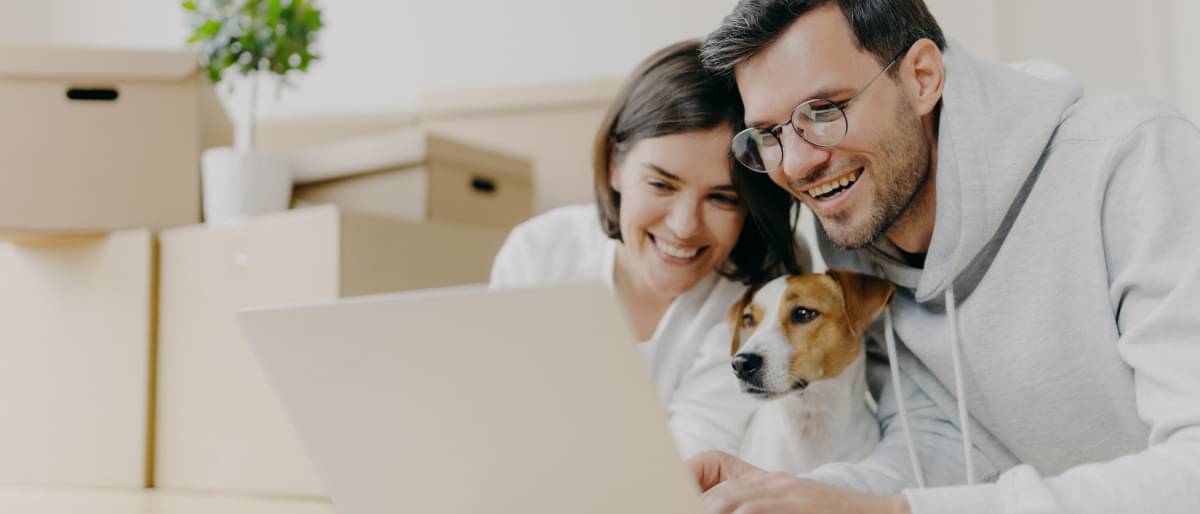 Lächelndes Paar mit Hund schaut auf den Bildschirm eines Laptops
